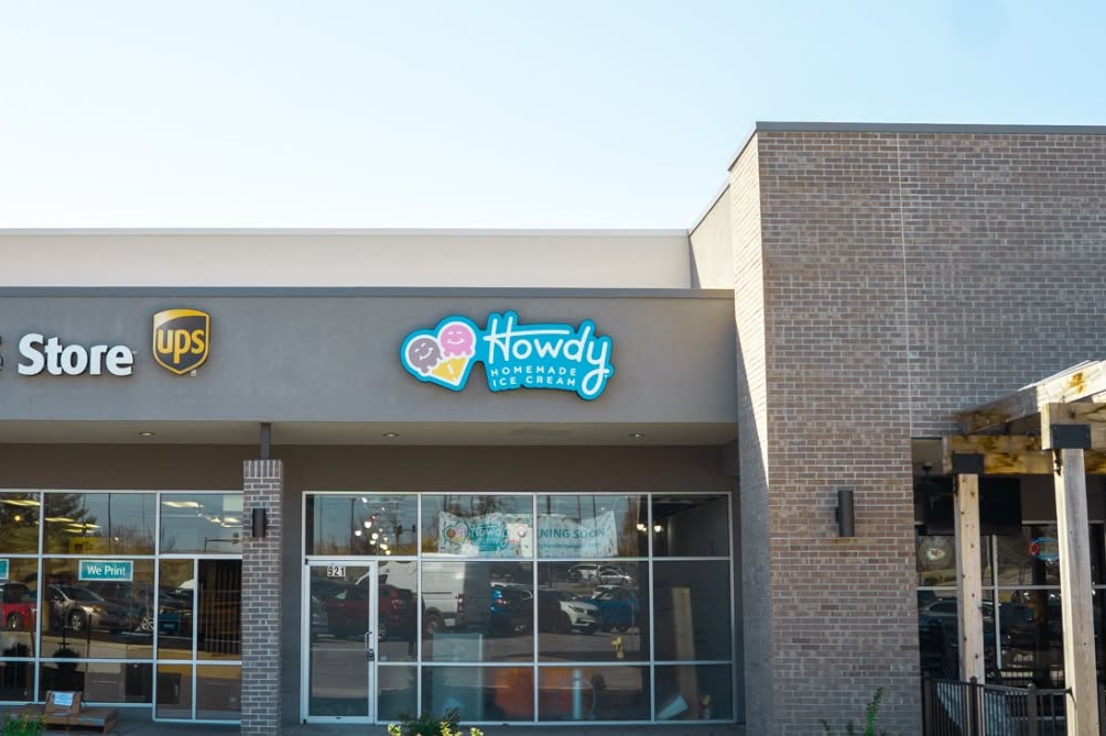 exterior of a brick building with glass window store front with a sign Howdy Homemade Ice Cream and a UPS sign to the left